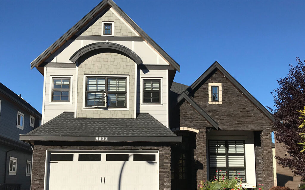 Two-storey cream home with a garage next to a dark brown brick home