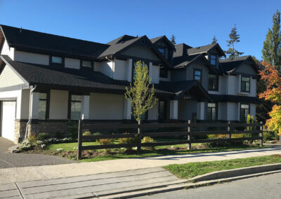 Dark home with a long fence and white-framed windows beside the street