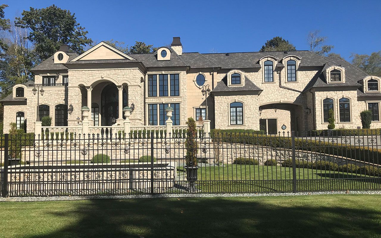 Large stone mansion with a wrought-iron fence and many windows