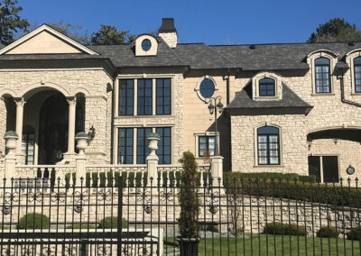 Stone mansion with arched windows behind a black iron fence