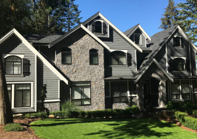 Stone and grey-siding home with several steep gables and a green lawn