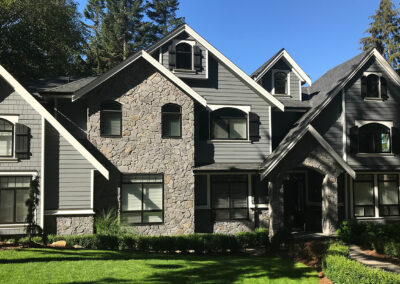 Stone and grey-siding home with steep gables, seen from another angle