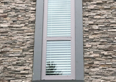 Tall narrow window with white blinds set between stone cladding panels