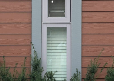 Narrow window with white blinds beside red panel siding