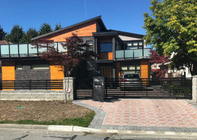 Modern home with orange and dark cladding, glass railings and a brick driveway