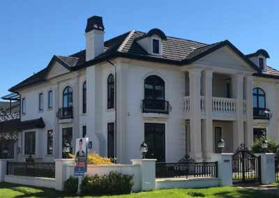 White classical mansion with arched windows, balconies and a gated driveway