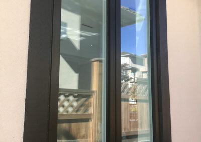 Tall dark-framed window reflecting a fence and trees