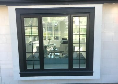 Large black-framed picture window with grid bars on a white wall, with a living room visible inside