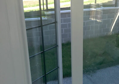 Close-up of a white window with grid bars overlooking a garden and wall