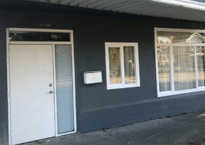 White entrance door with a sidelight and white-framed windows on a dark grey wall