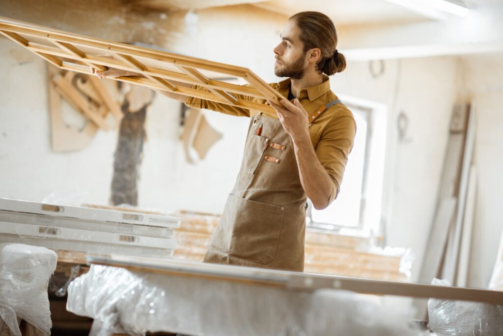 Craftsman lifting a wooden window frame inside a home