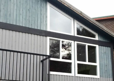 Grey-blue cedar-sided home with large white-framed windows and a black railing